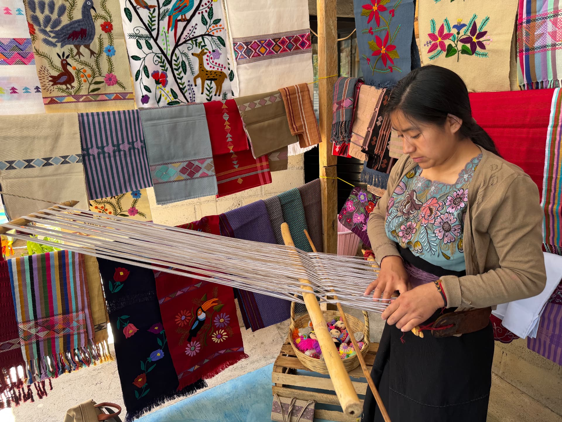 Artisan weaving on a backstrap loom surrounded by hand-embroidered textiles